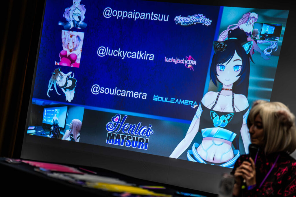 Photo of a large projection screen with a VTuber and person hosting a panel together